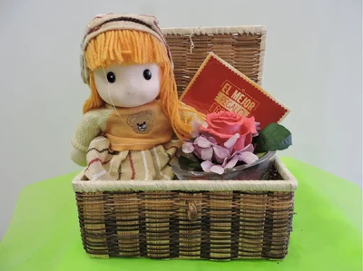 Cesta mimbre con muñeca, bombones y rosa deshidratada